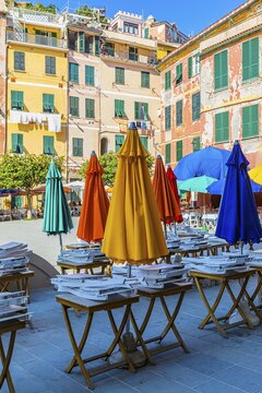 Coloured parasols of a closed restaurant at the main square of Vernazza, behind them pastel-coloured house facades, Vernazza, Cinque Terre, Ligurian Coast, Liguria, Italy