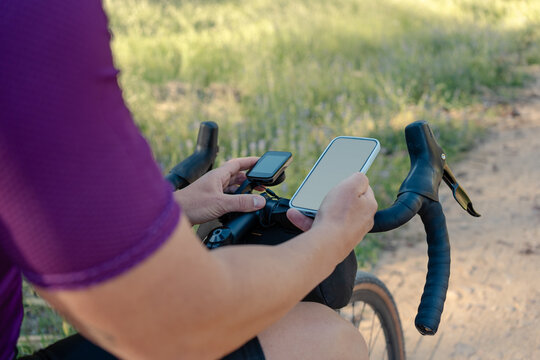 Cyclist checking smartphone and cycling computer navigation on gravel route