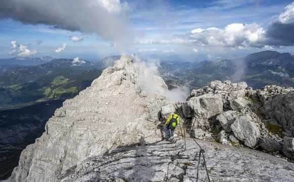 Climber on a via ferrata secured with steel rope, narrow rocky ridge, Watzmann crossing to Watzmann Mittelspitze, view of mountain panorama, Berchtesgaden National Park, Berchtesgaden Alps, Bavaria, Germany