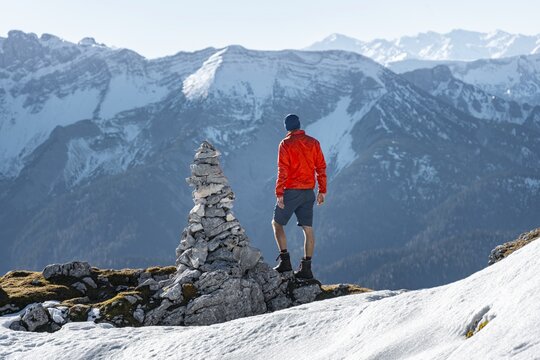 Mountaineer next to a cairn, in front of snowy mountains of the Rofan, hiking trail to the Guffert with first snow, in autumn, Brandenberg Alps, Tyrol, Austria