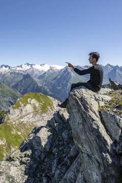 Mountaineer sitting on a rock, pointing to a mountain peak, mountain panorama with Gro&szlig;venediger, mountain landscape with mountain peaks of the Venediger group, view from the summit of the G&ouml;sleswand, Las&ouml;rling group, Hohe Tauern National Park, East Tyrol, Tyrol, Austria