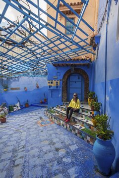 Young woman in the old town sits on a staircase, blue house walls, medina of Chefchaouen, Chaouen, Tangier-T&eacute;touan, Kingdom of Morocco