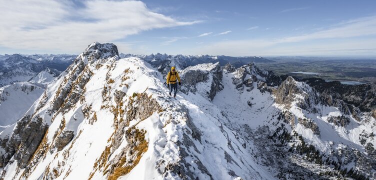 Climbers on a narrow rocky snowy ridge, behind peak crow, view of mountain panorama, hiking to Ammergauer Hochplatte, in autumn, Ammergau Alps, Bavaria, Germany