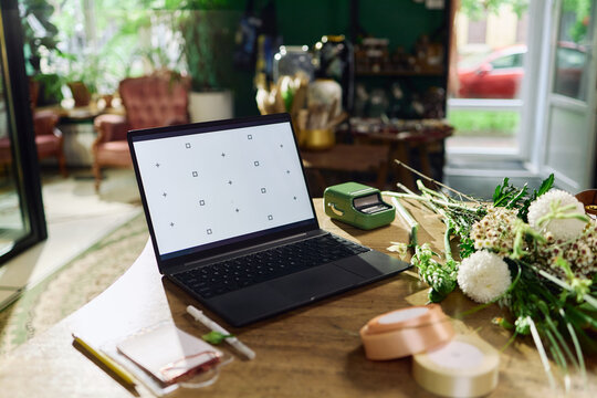 Wide shot of laptop displaying mockup screen beside bouquet assembly tools on worktable, supporting florist e commerce workflow. Ideal for online shop, small business branding, website banner