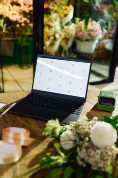Vertical shot of laptop displaying blank mockup screen on florist worktable, supporting online shop management and digital marketing. Ideal for ecommerce, branding, website banner use