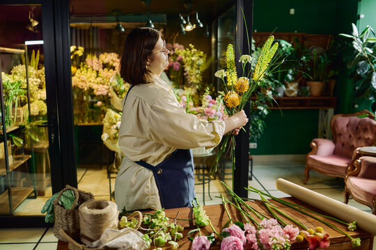 Side view of Caucasian woman arranging flower bouquet in florist shop, creating retail product display for gifting and event decor marketing