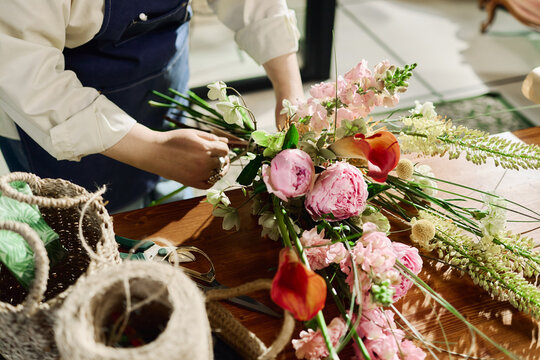 Close up of unrecognizable woman arranging flower bouquet on worktable, creating handcrafted floral product for retail sale. Ideal for florist business, small shop marketing, ecommerce
