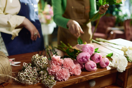 Women arranging fresh flowers on worktable, preparing bouquet design in florist studio. Supporting floral business, retail marketing, handmade product branding, close up