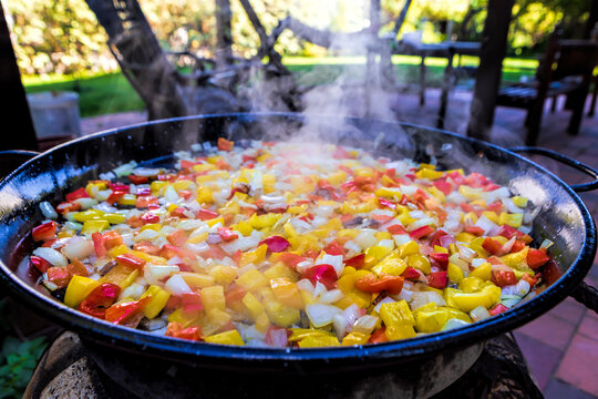 Cooking traditional spanish paella sofrito with chopped peppers and onions outdoor