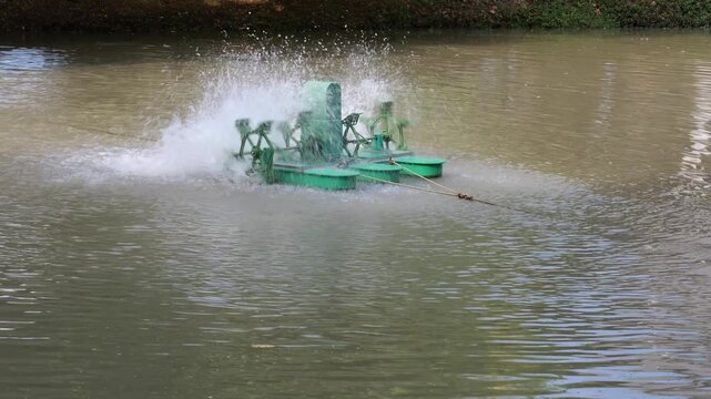 Water paddle wheel aerator machine operating on a pond, splashing water to increase oxygen levels for aquaculture and fish farming, captured in natural daylight.