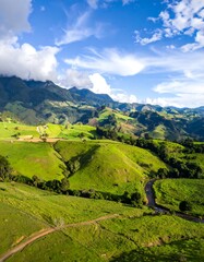 Naklejka premium Lush green rolling hills with winding road and distant mountains