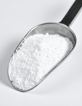 Tiny metallic scoop with pure white titanium dioxide powder. Isolated on sterile white background. Close-up.