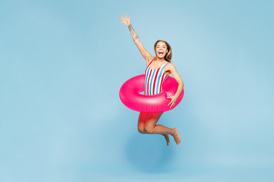 Full body profile young fun woman wears bikini swimsuit pink rubber ring rest near hotel pool jump high into water raise up hand isolated on plain blue background. Summer vacation sea sun tan concept.