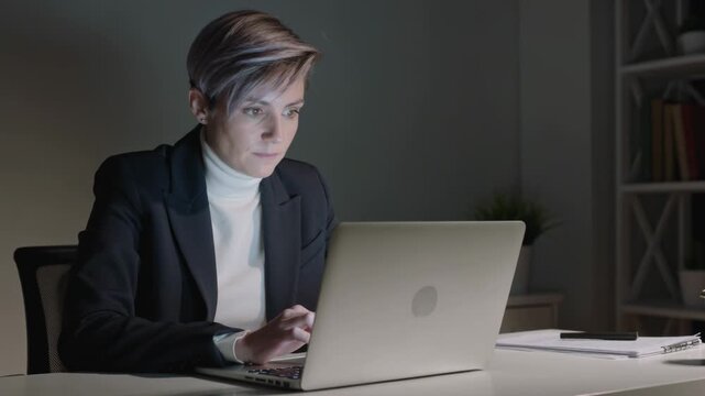 Typing blazer-clad worker prompted by alert on silver laptop, speaking and entering data at desk