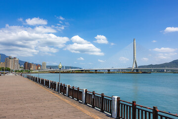Fototapeta premium Wooden seaside walkway overlooking modern Danjiang Bridge in Tamsui Taiwan