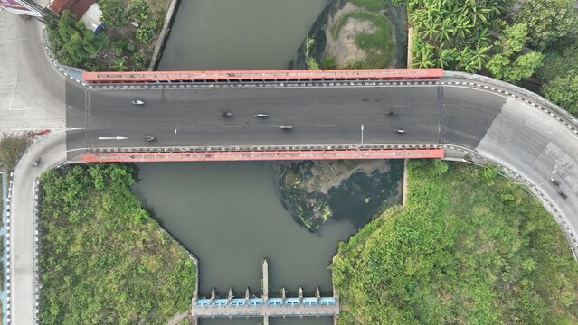 Aerial view of a bridge spanning a river with lush green vegetation and road infrastructure in Bekasi Barat, West Java, Indonesia.