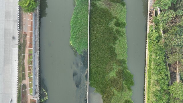 Aerial view of a canal with dense green vegetation and concrete banks in Bekasi Barat, West Java, Indonesia.