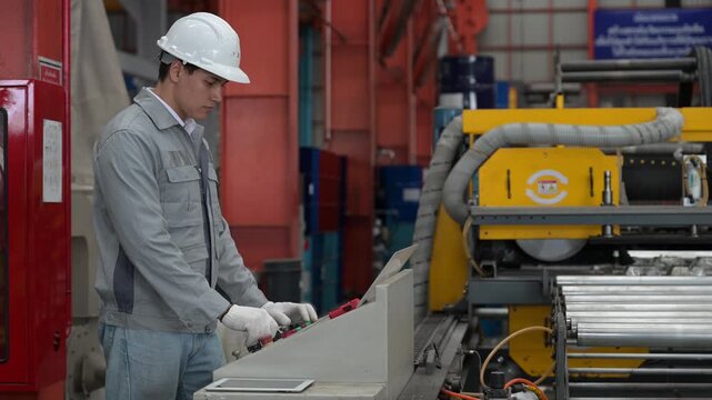 Professional industrial engineer wearing safety helmet and uniform standing beside the conveyor line and inputting operation commands on the technical control desk board.