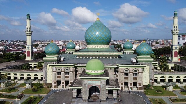 Aerial view of An-Nur Great Mosque with its distinctive green domes and minarets set against the urban skyline of Pekanbaru, Riau, Indonesia.
