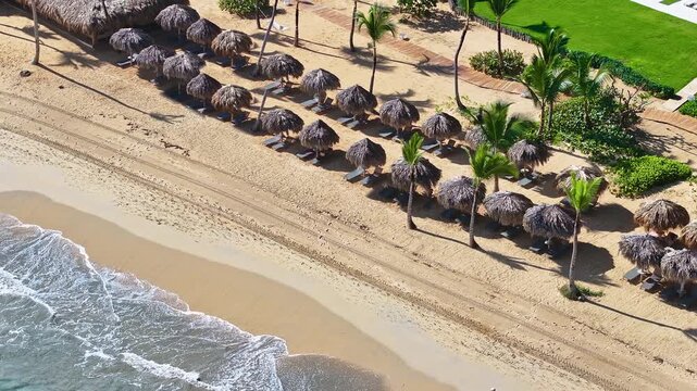 Beautiful view of the beach line with thatched umbrellas and the ocean. Yellow sand and clear waves. A resort beach on a golden shore on a clear day. Travel and summer vacation concept background.