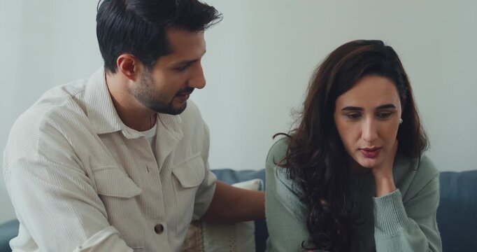 Young Hispanic husband comforting sad depressed wife on sofa in home living room. Mental health support, marriage couple conflict problem, grief emotion therapy, family trauma crisis concepts.