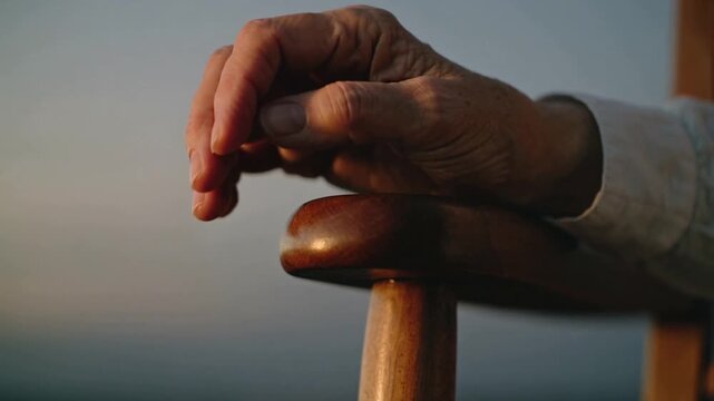 Relaxing senior hand sliding varnished deck rail over sea as sun warming skin, showing light cuff