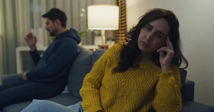 Stressed Hispanic young couple anger ignoring each other and sit apart on sofa at home night. Marriage relationship problem, domestic conflict stress, divorce crisis, communication breakdown concept.