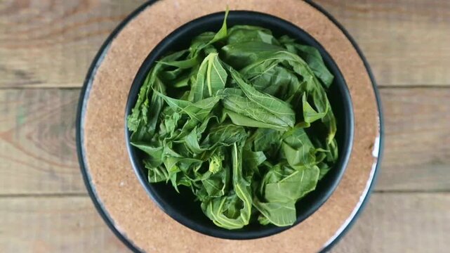 Close up Boiled Cassava Leaves in Black Bowl, turning. Rotation display