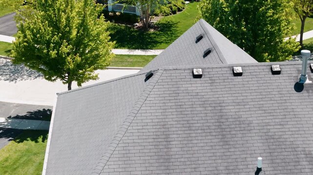 Aerial shoot of a residential house roof with asphalt shingles, roof vents, and modern roofing construction in a suburban neighborhood.
