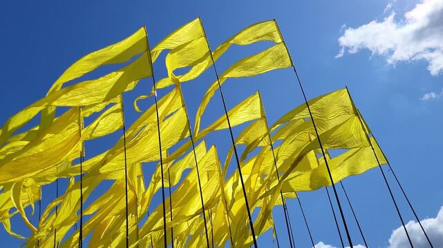 Yellow flags fluttering in wind against blue sky. Row of vibrant textile banners for outdoor event decoration. Celebration concept, festive atmosphere and dynamic movement in bright sunlight.