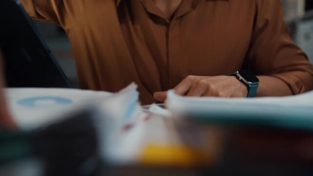 Close up overworked young Latin businessman working late on document in large stack of paper files at office night. Tax audit deadline, accounting stress, corporate burnout, urgent business concept.
