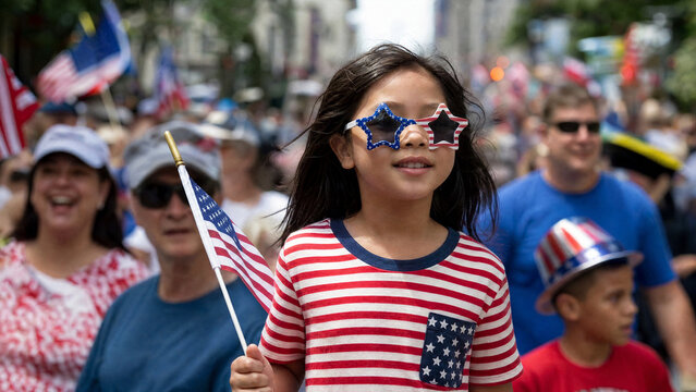 Happy young girl in patriotic clothing holding an American flag at a street parade, celebrating Independence Day or Memorial Day with family and community during summer
