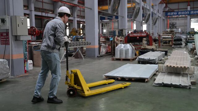 Male Factory Worker Transporting Materials with Pallet Jack in Industrial Plant.