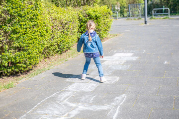 Fototapeta premium Child playing hopscotch on sunny day, legs of a girl in jeans and sneakers jumping on chalk squares on pavement, active outdoor traditional games, childhood fun, back to school leisure, happy girlhood