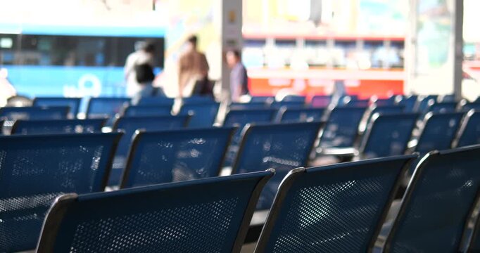 Rows of blue chairs in bus terminal with blurry buses background
