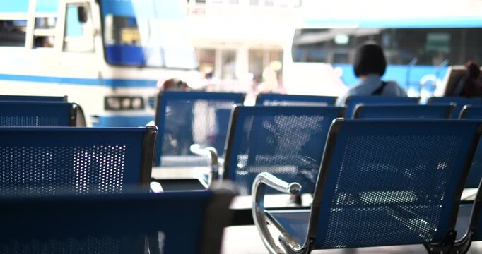 Rows of blue chairs in bus terminal with blurry buses background