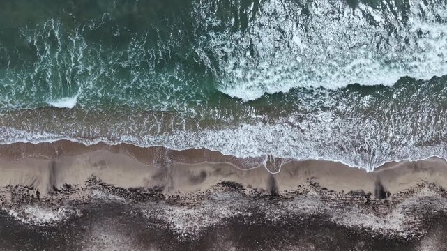 Waves crash onto the shore as the tide comes in, mixing water and sand at a beach location in the morning sun. The patterns of the surf create a natural design at the edge of the sea.