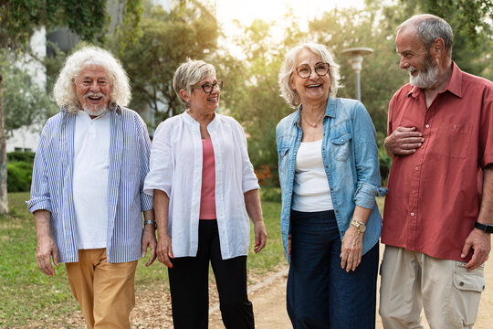 Happy senior friends walking together in public park enjoying fun conversation during retirement