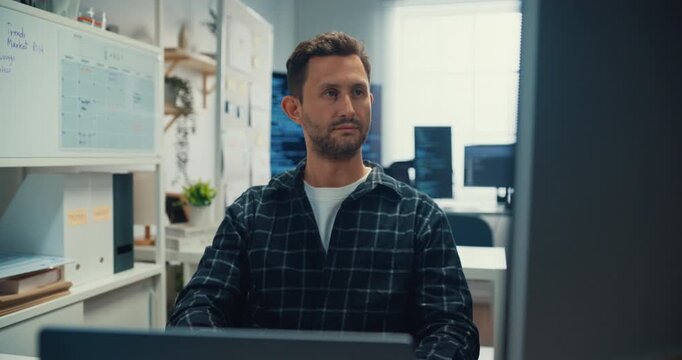 Young Caucasian male programmer writes code using multiple screens in home office workspace. AI development, cybersecurity, network database system, software engineering, remote tech startup concept.