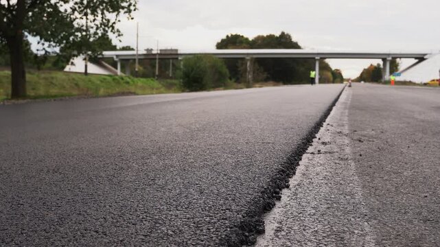 Fresh, hot asphalt laid on a highway during construction. Low-angle close-up of the new pavement surface during road repair operations