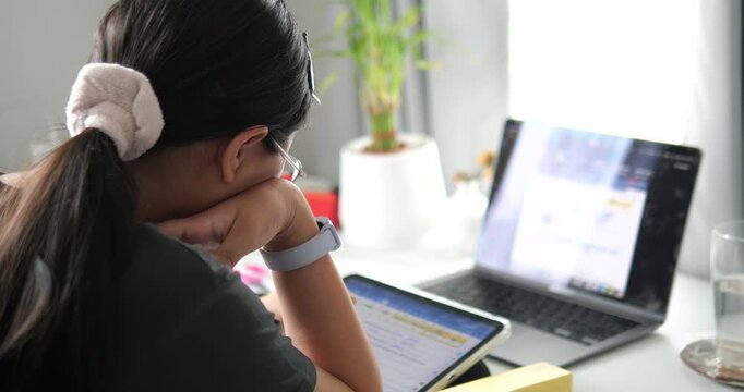 Rear view of young Asian woman thinking and working at desk