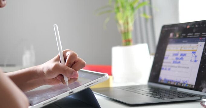 Close up of hand writing on tablet with laptop on desk