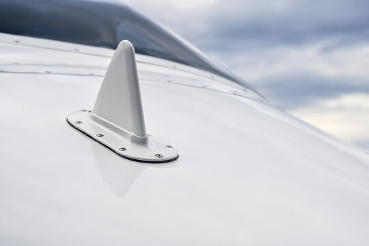 Close up of VHF communications antenna mounted on white aircraft fuselage against cloudy sky