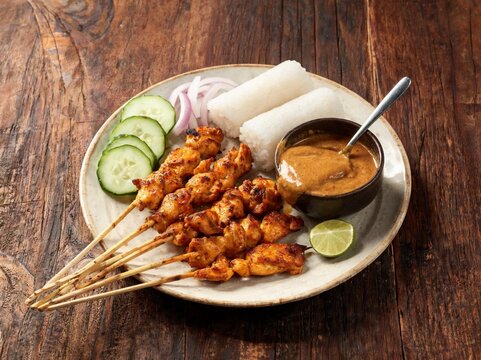 Indonesian Chicken Satay Sate Ayam with Peanut Sauce Lontong Cucumber and Lime on Wooden Background