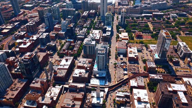 Overhead view of city grid and elevated rail, Chicago, Illinois. Drone perspective of rooftops, street intersections, parking lots and an L train viaduct in afternoon light.
