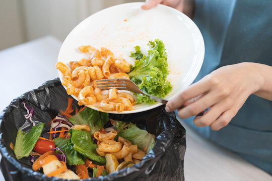 Compost from leftover food asian young housekeeper woman, girl hand holding macaroni plate use fork throw away food scraps, rotten vegetable into trash. Environmentally responsible, food waste concept