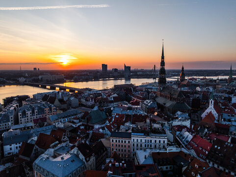 Aerial view of Vecriga, the historic old town of Riga, featuring the iconic spire of St. Peters Church, dense rooftops, and the Daugava River under a vibrant sunset sky in Riga, Latvia.