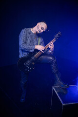 Fototapeta premium Adult male musician with skeletal face paint playing electric guitar in blue stage lighting
