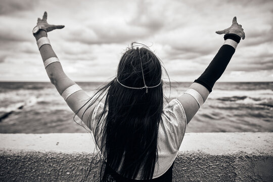 Young woman cosplay character with long black hair raising hands by stormy seaside