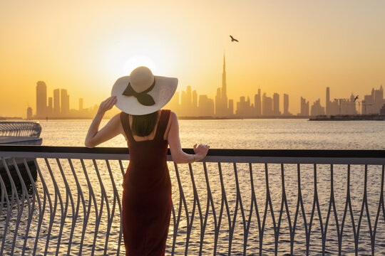 A beautiful woman stands at Creek Harbour and looks at the distant skyline of Dubai, UAE, during sunset